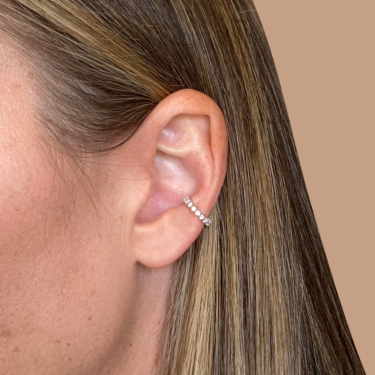 Close-up of a person's ear with a diamond stud earring on a beige background